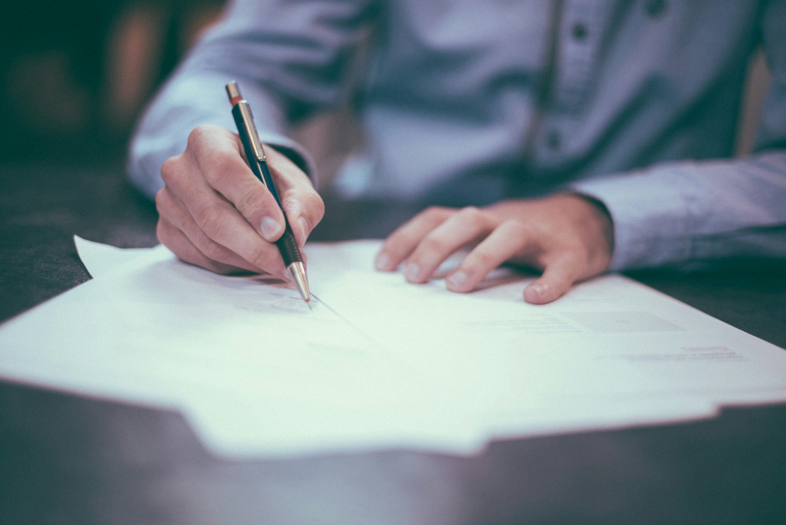 person writing on paper with a pen on a table
