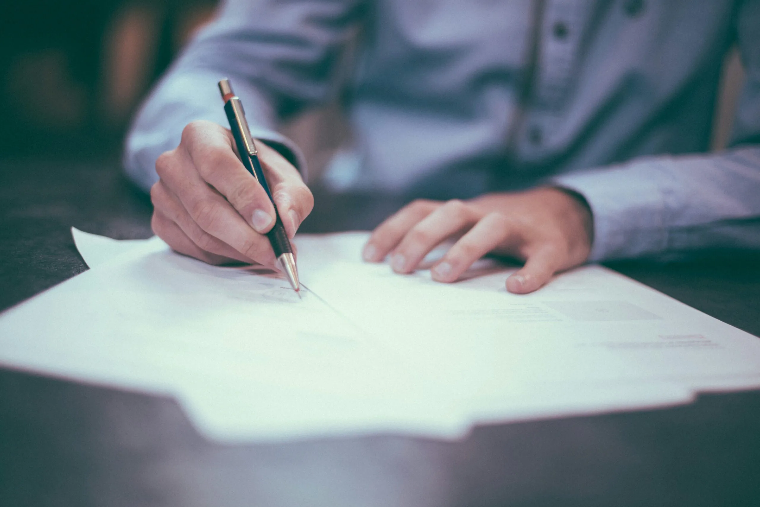 person writing on paper with a pen on a table